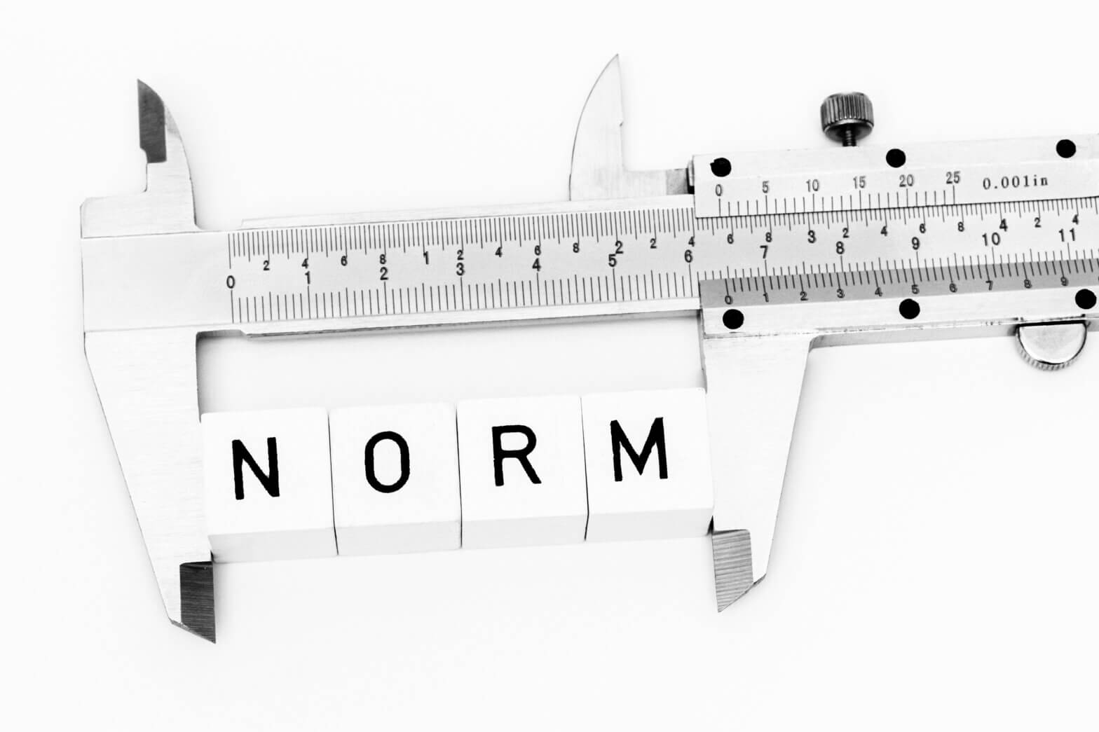 Ein Messschieber misst vier Würfel mit Buchstaben die zusammen das Wort Norm bilden
